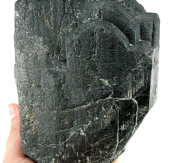 A large natural tantalite mineral specimen, held in a hand for scale.