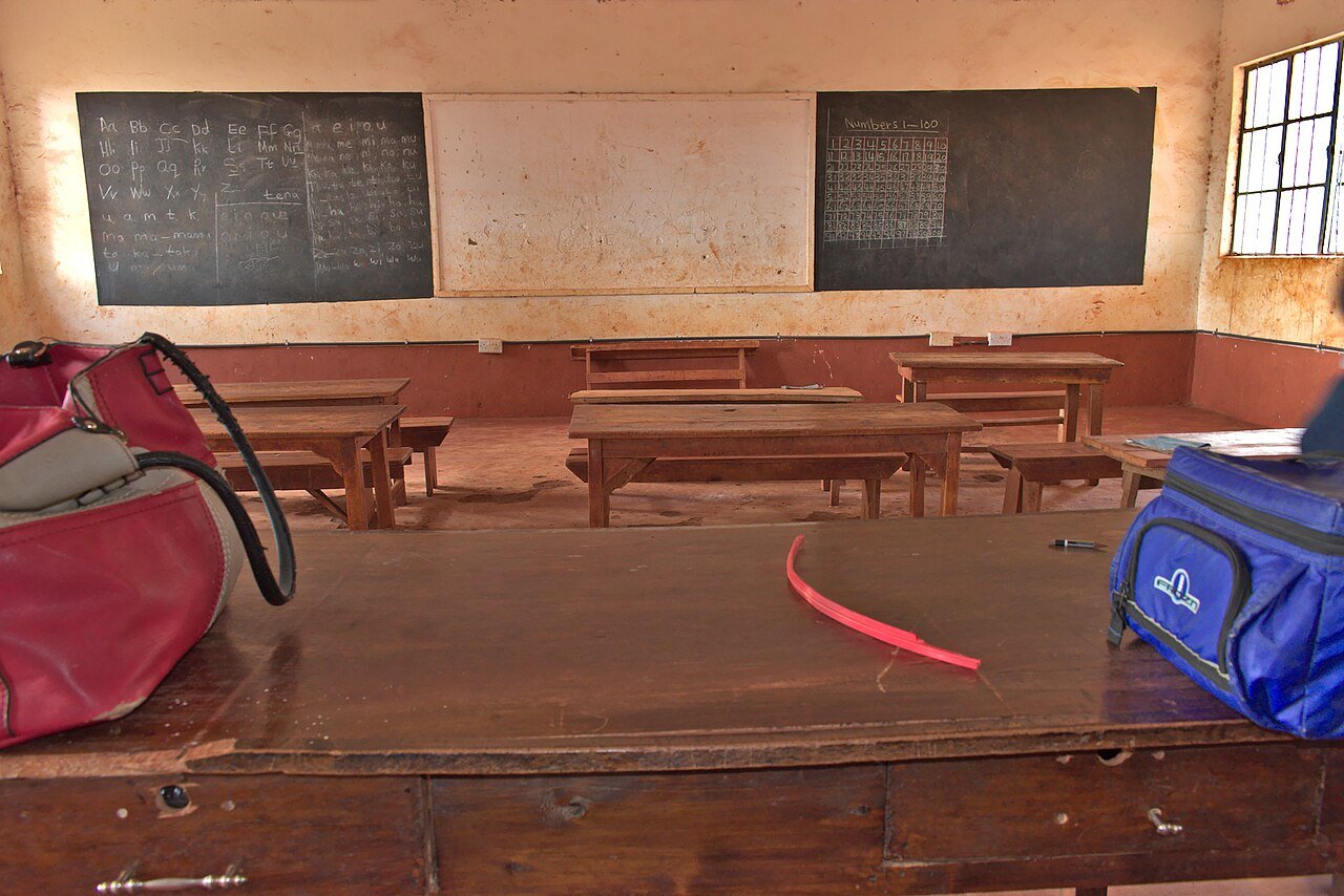 An empty Kenyan classroom with wooden desks and blackboards; representative education photography.