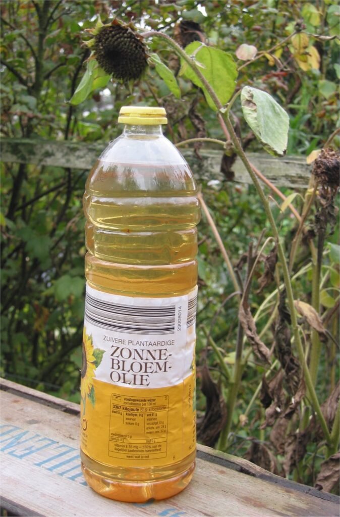 A bottle of sunflower oil photographed beside sunflower plants.