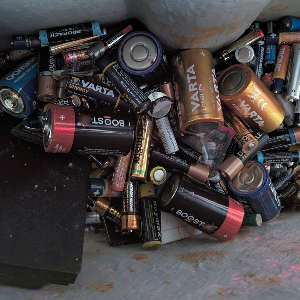 Used household batteries collected inside a recycling container.