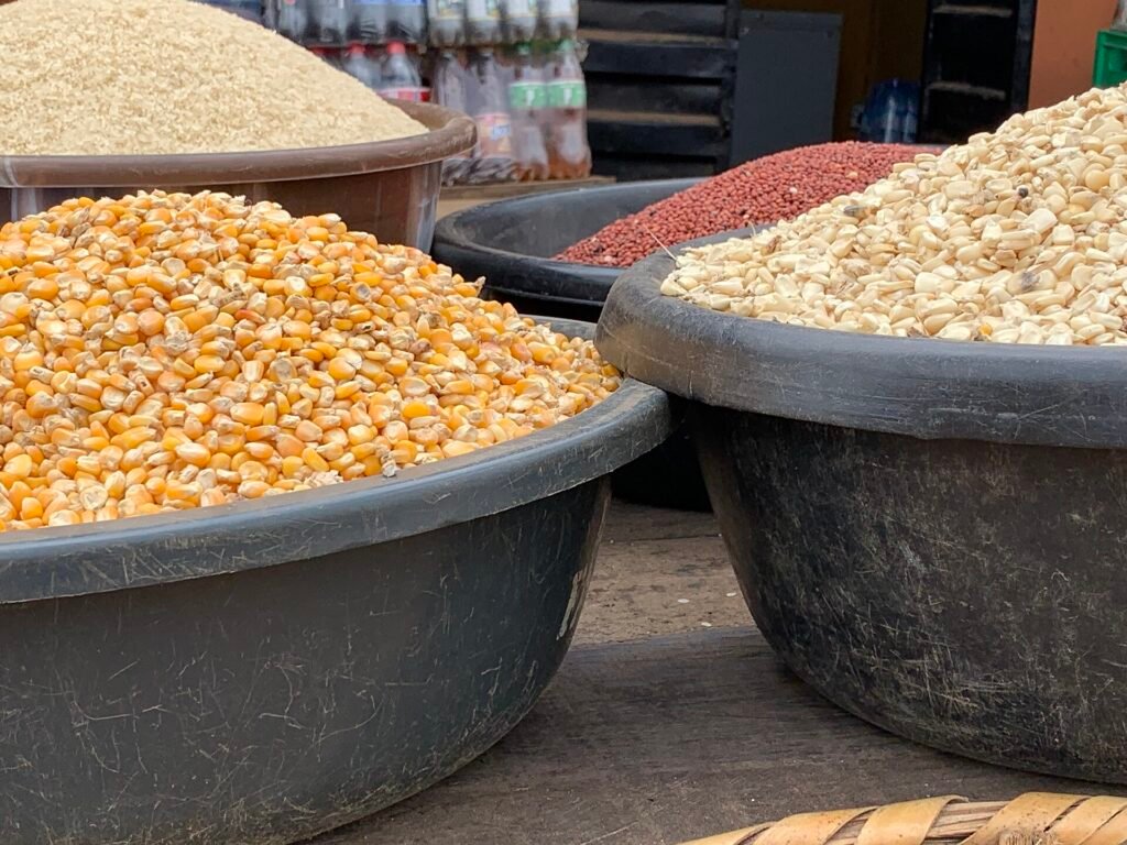Yellow and white maize kernels in containers at a market; yellow maize is visible in the foreground.